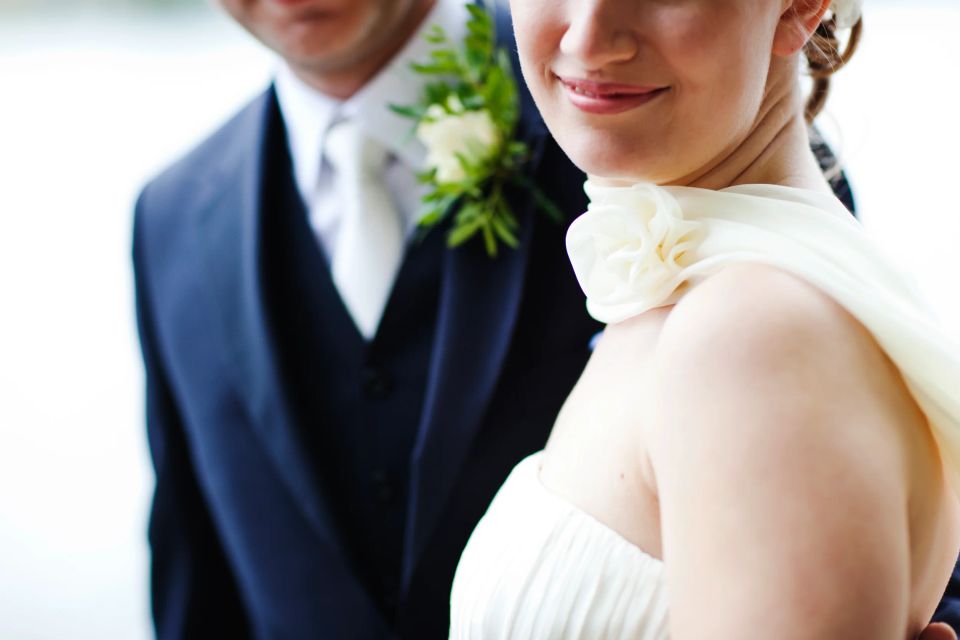 Bryllupsfotografi: Brudepar med fokus på bruden der smiler i hvid kjole og brudgom i mørkt jakkesæt med bryst