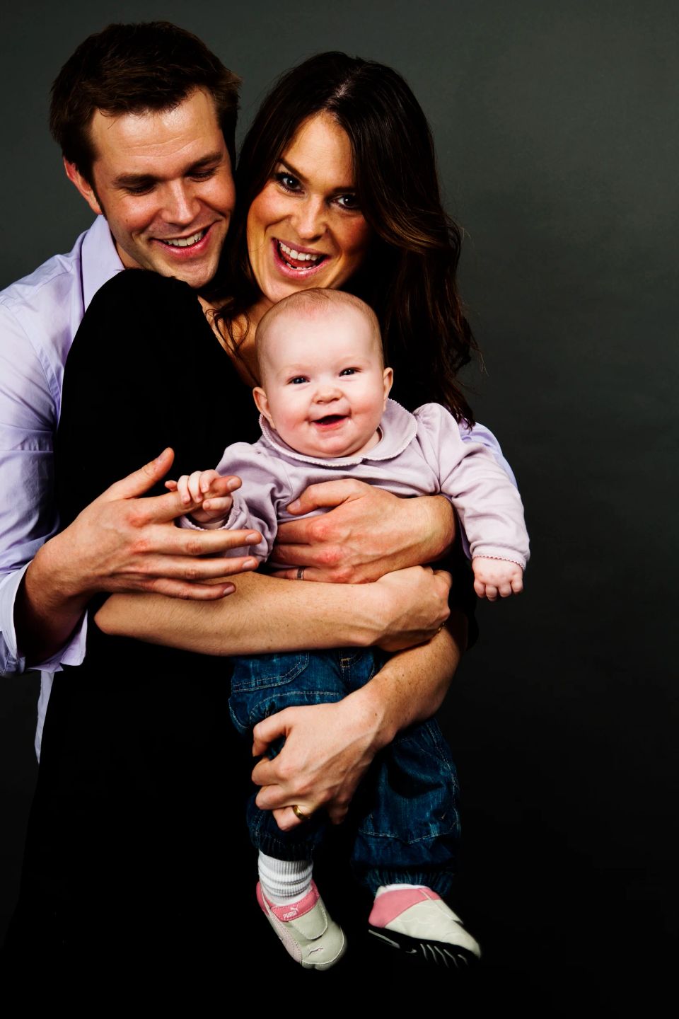 Familieportræt af glade forældre der holder deres grinende baby i et spontant og varmt øjeblik, fotograferet i Virum.