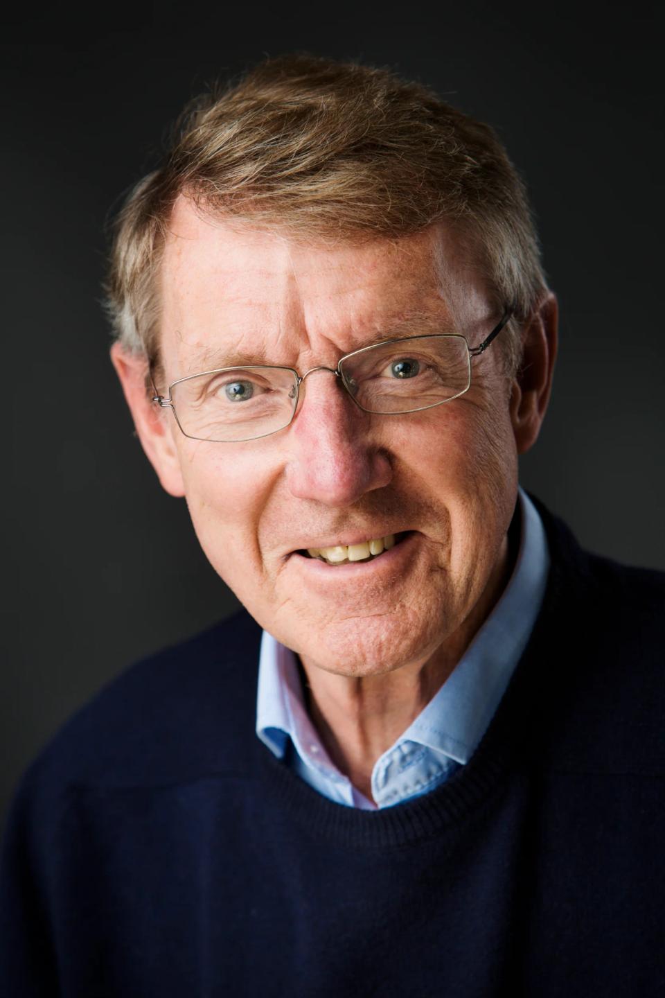 Portrætfoto af ældre mand med briller og et varmt, autentisk smil mod en mørkere, blød baggrund.
