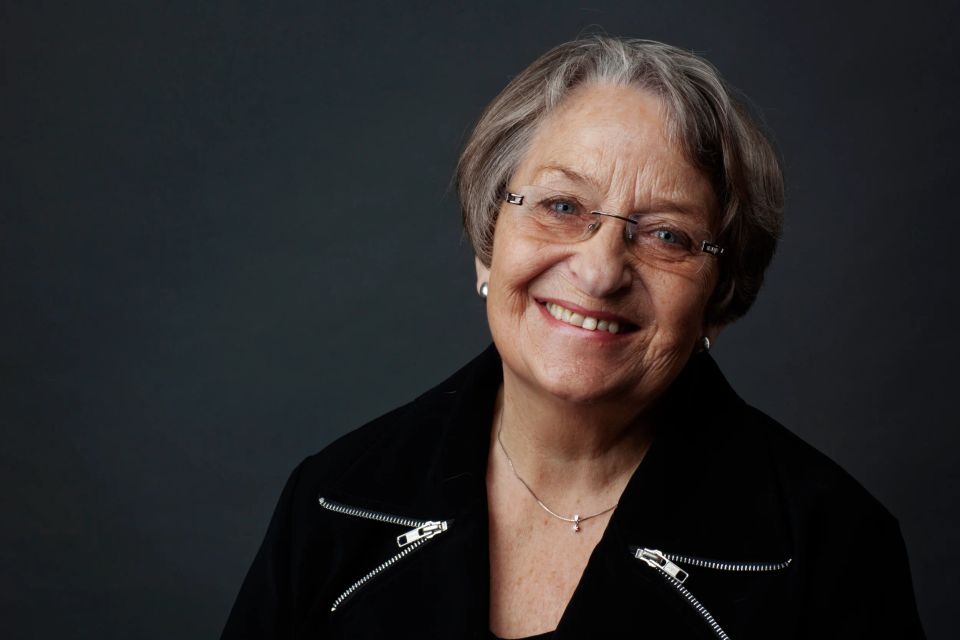 Professionelt portrætfoto i sort/hvid af en smilende kvinde med briller og kort gråt hår i skarpt lys.