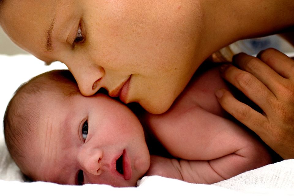 Nærbillede af en mor, der ømt kysser sin nyfødte baby på panden. Et smukt øjeblik af kærlighed i dette babyfotografi.