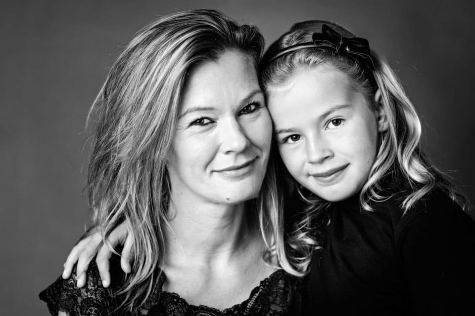 Familiefoto i sort-hvid af mor og datter der smiler. Datter står tæt ind til mor med hånden på hendes skulder.