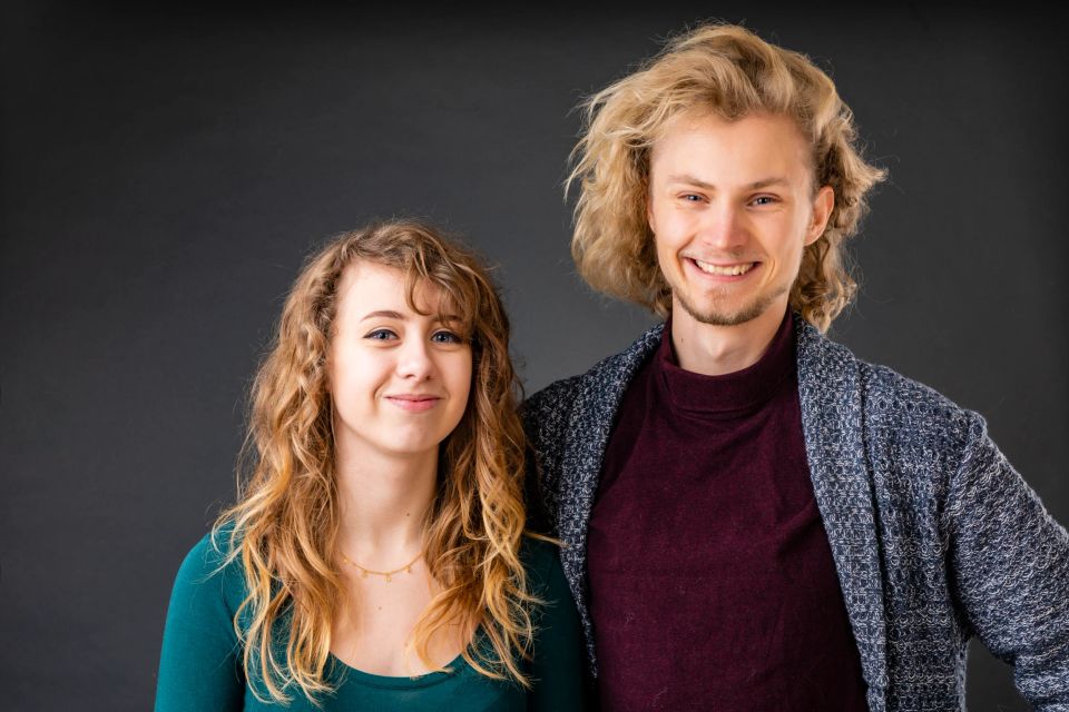 Familieportræt af smilende søskende med lyst krøllet hår foran mørk baggrund i naturligt lys.