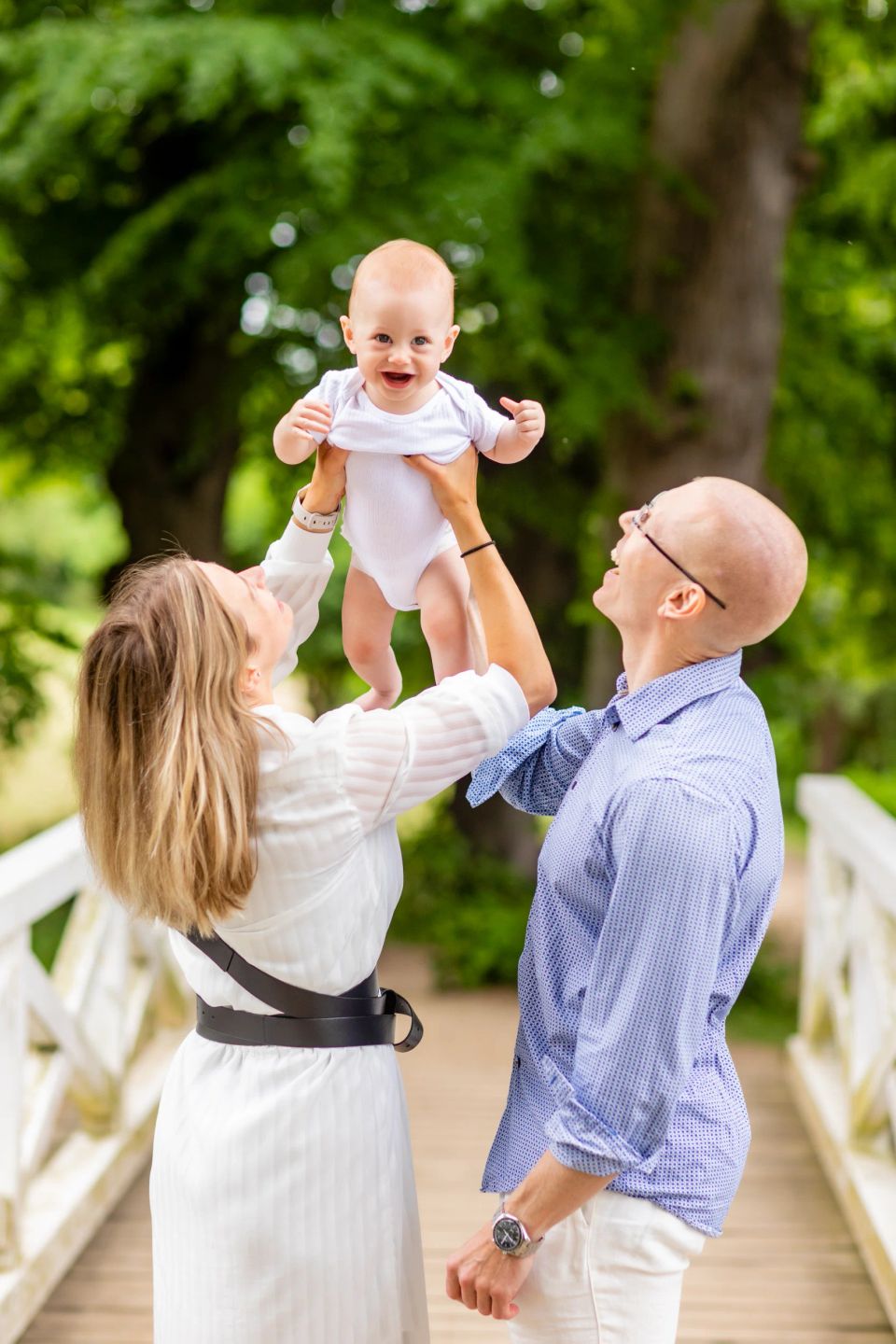 Familiefotografering hvor mor og far griner og holder deres glade baby op i luften udendørs i Virum.