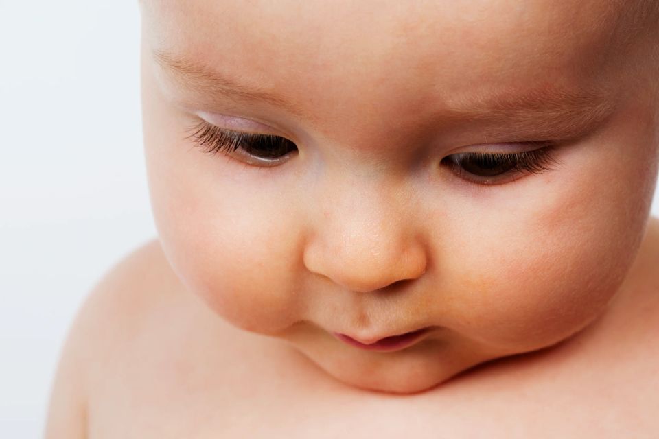 Nærportræt af baby med tænksomt udtryk, set skråt fra oven med blødt, diffust lys. Et roligt babyfotografi.