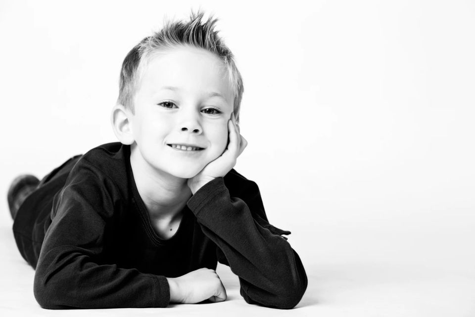 Sort-hvid fotografering af glad dreng med sjov frisure, som ligger afslappet og smiler mod beskueren.