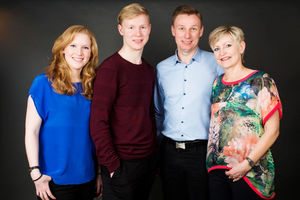 Familiefotografering i Virum: fire smilende voksne i farverigt tøj foran en mørk baggrund. Glade familiebilleder.