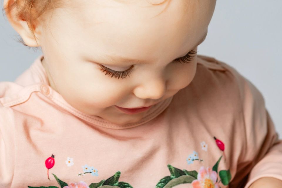 Nært babyportræt med fokus på ansigtet, lukkede øjne og søde kinder. Baby har en ferskenfarvet bluse med blomster på.