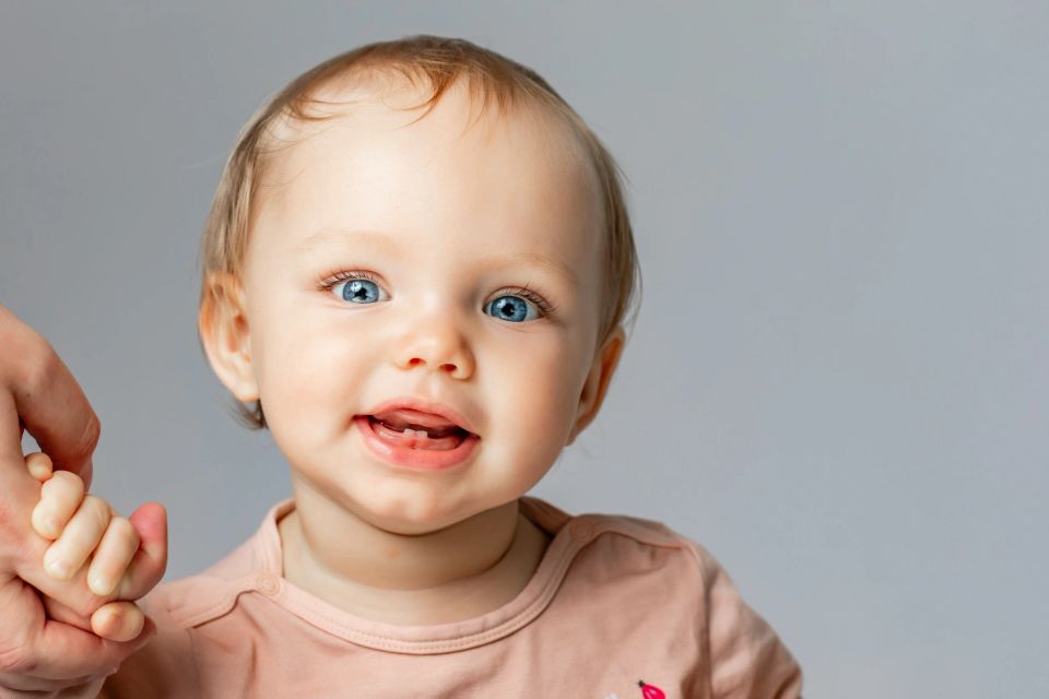 Glad baby med strålende blå øjne holder en voksen i hånden. Et naturligt babybillede i blødt lys.